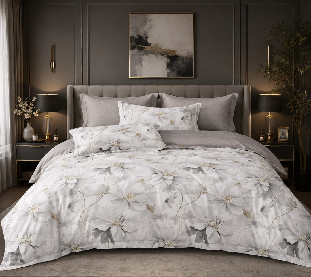 A styled beddings set showing a bed made up with a white duvet cover and matching pillow shams featuring a large floral print in soft gray and beige tones. 