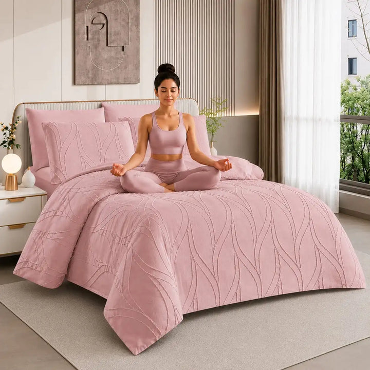 A woman in a pink activewear set sits cross-legged on a bed with a matching pink quilted 200x200_duvet_cover_set in a modern bedroom.