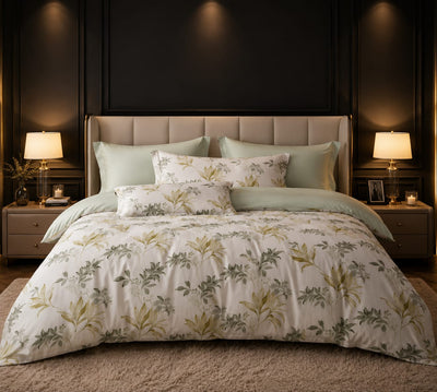 A neatly made bed in a styled bedroom setting, featuring a bedsheet king size white
 and matching pillow shams with a botanical leaf pattern in muted green and beige on an off-white background. The bed is styled with solid sage green pillows and a beige upholstered headboard is visible behind it.