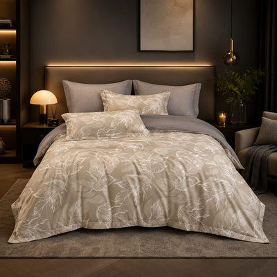 A neatly made bed in a modern bedroom setting, featuring a beige and gray botanical pattern duvet cover set and matching pillow shams, styled with gray pillows and a gray throw blanket.